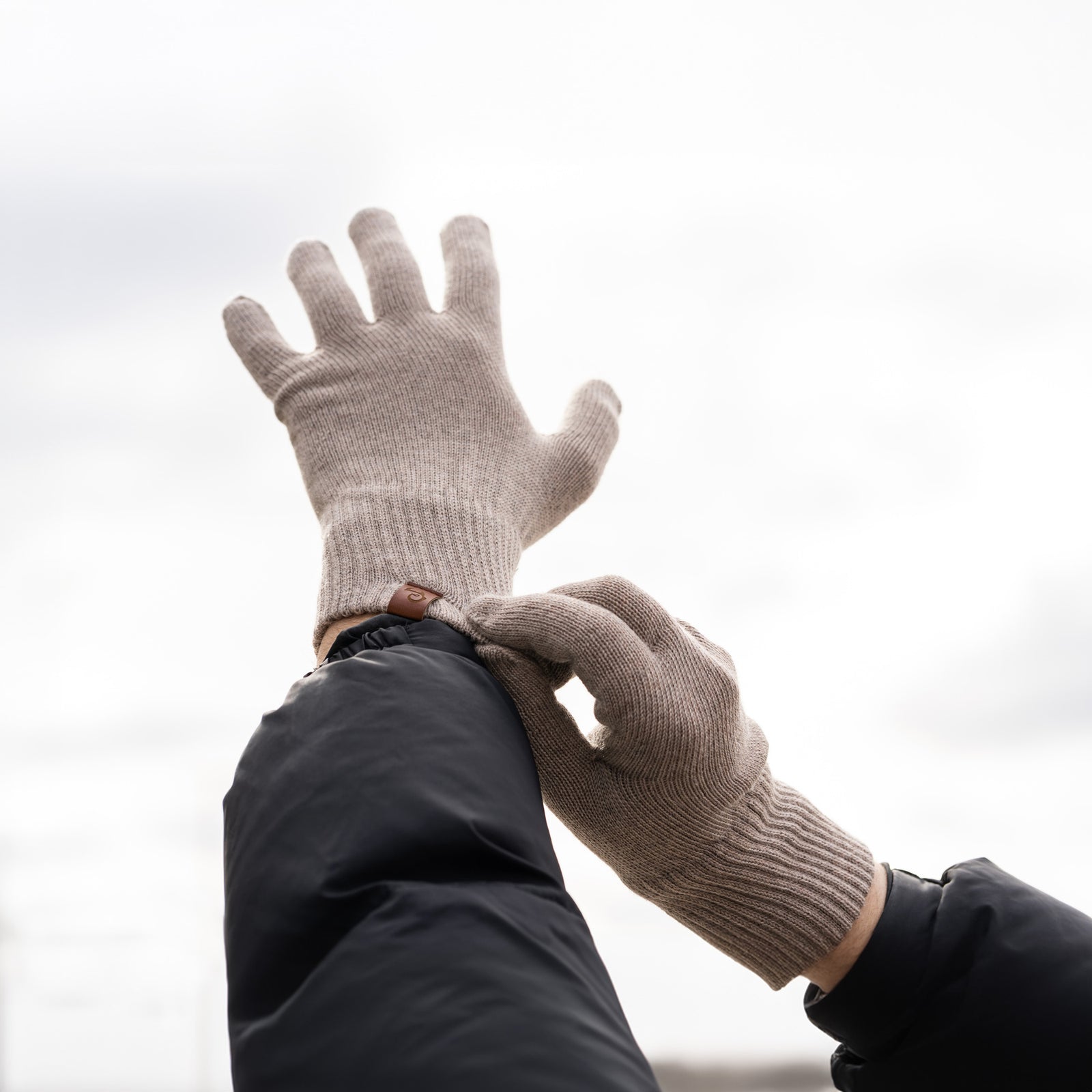 A person wearing black knit gloves from menique, while sitting on a wooden bench outdoors. The gloves appear to be snug-fitting and warm.