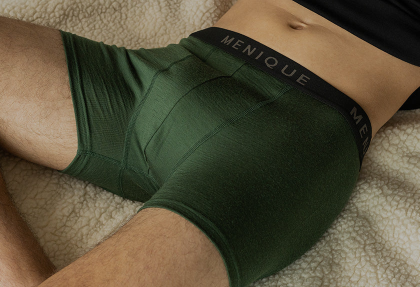 Person wearing green underwear with 'Menique' brand label on a textured surface