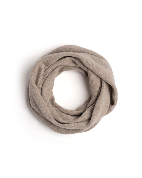 A beige knit infinity scarf coiled into a neat circle on a white surface.