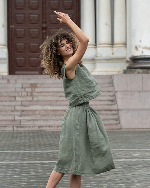 Woman with a curly hairstyle posing in a city, wearing stone green crop top and stone green skirt Sophia.