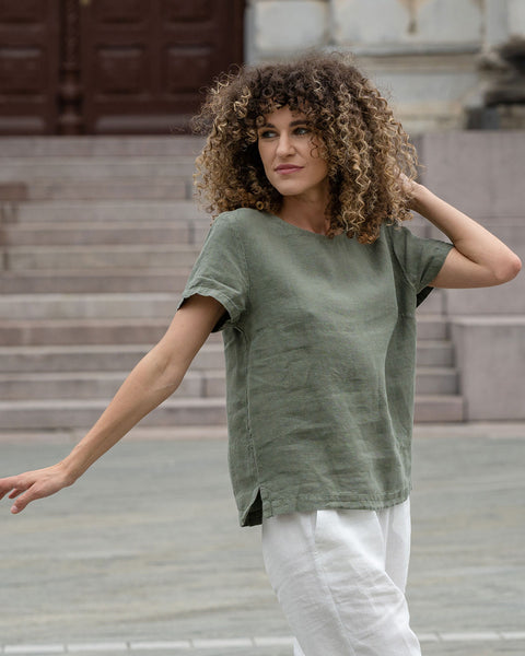 Beautiful woman with a curly hair in the city, posing wearing stone green linen blouse Emma and pure white linen pants Dakota.