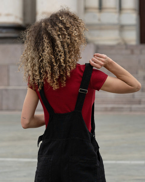 Beautiful woman with curly hair posing from the back in the city wearing pure black linen jumpsuit Nicci, royal cherry merino wool top.