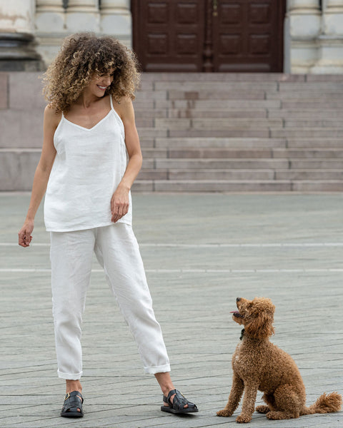 Beautiful woman posing in a city. Wearing pure white linen slip top and pure white linen pants. With a brown poodle dog.