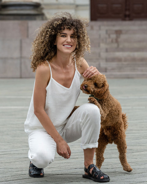 Beautiful woman posing in a city. Wearing pure white linen slip top and pure white linen pants and with a brown poodle dog.
