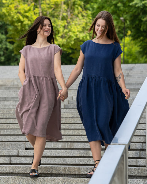 Two girls walking in the city holding hands, wearing linen smock dress cecilia, one in faded rose color, other in storm blue color.