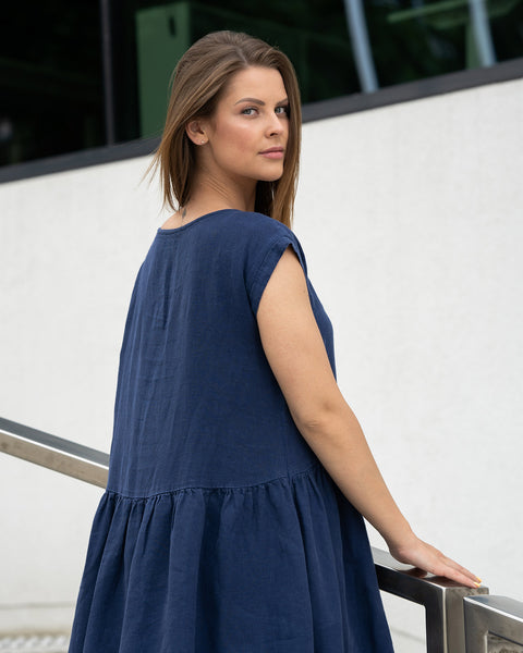 Young woman posing from the back in a city street on stears wearing linen smock dress cecilia in a storm blue color.