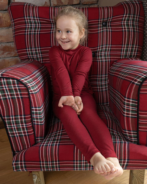 a girl sitting in a red checkered pattern armchair, wearing the menique Kids&#39; Merino 160 Long Sleeve Crew in Royal Cherry Color.